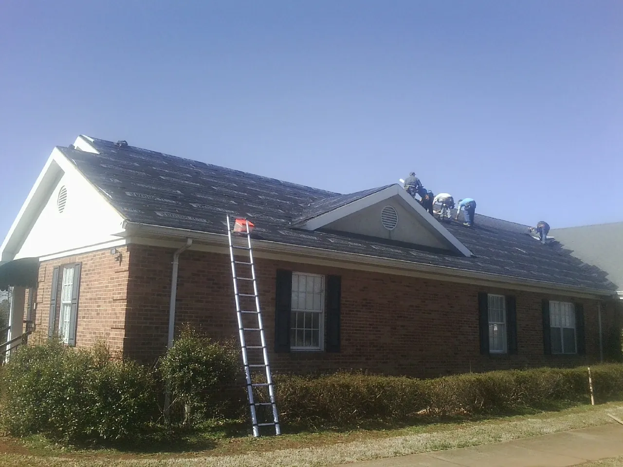 Crew tearing shingles off a brick ranch roof with a ladder set — Emergency Roof Repair work by our crew in Waterloo